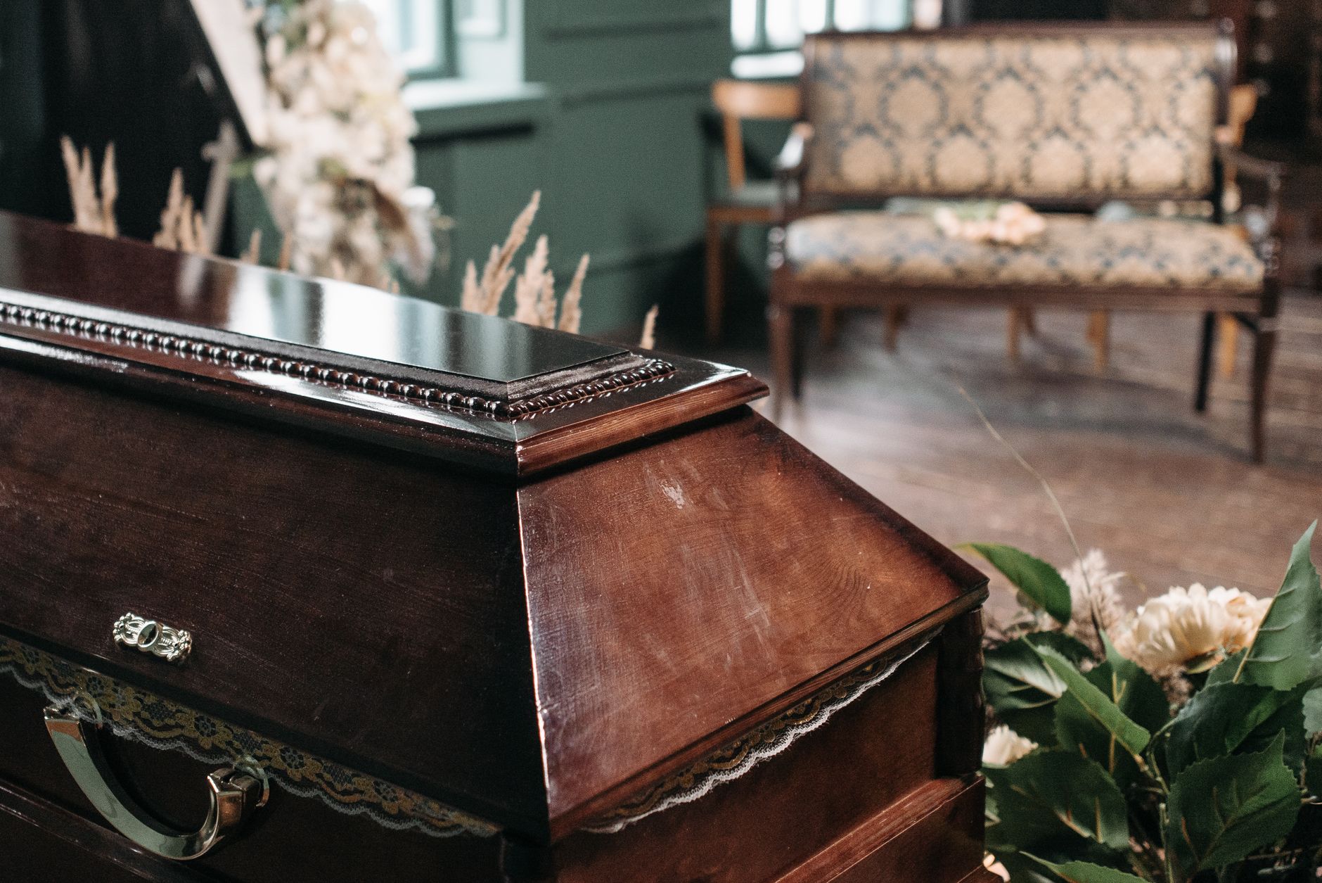 A dignified wooden casket surrounded by floral arrangements